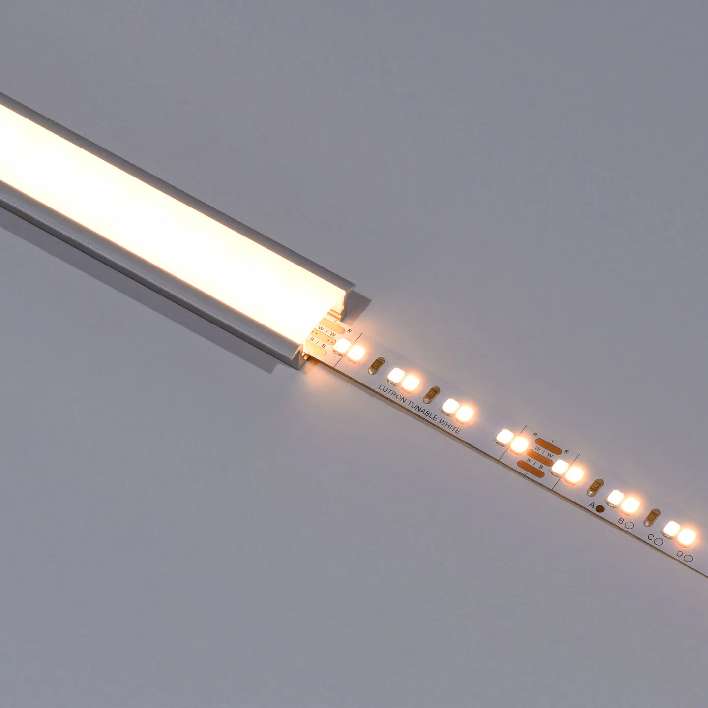 Close-up of a white LED strip with warm LEDs lit at the end, laid on a pale surface.