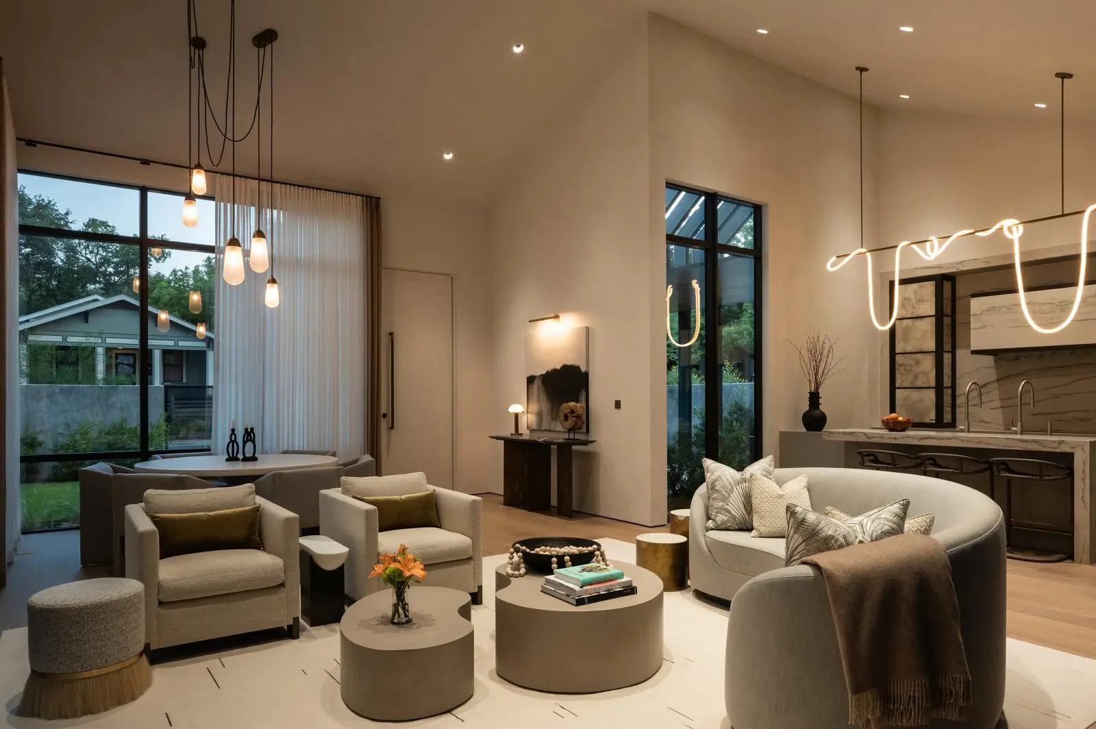 Modern open-plan living room with gray seating, round coffee tables, and a kitchen area featuring a glowing neon light sculpture along the ceiling.