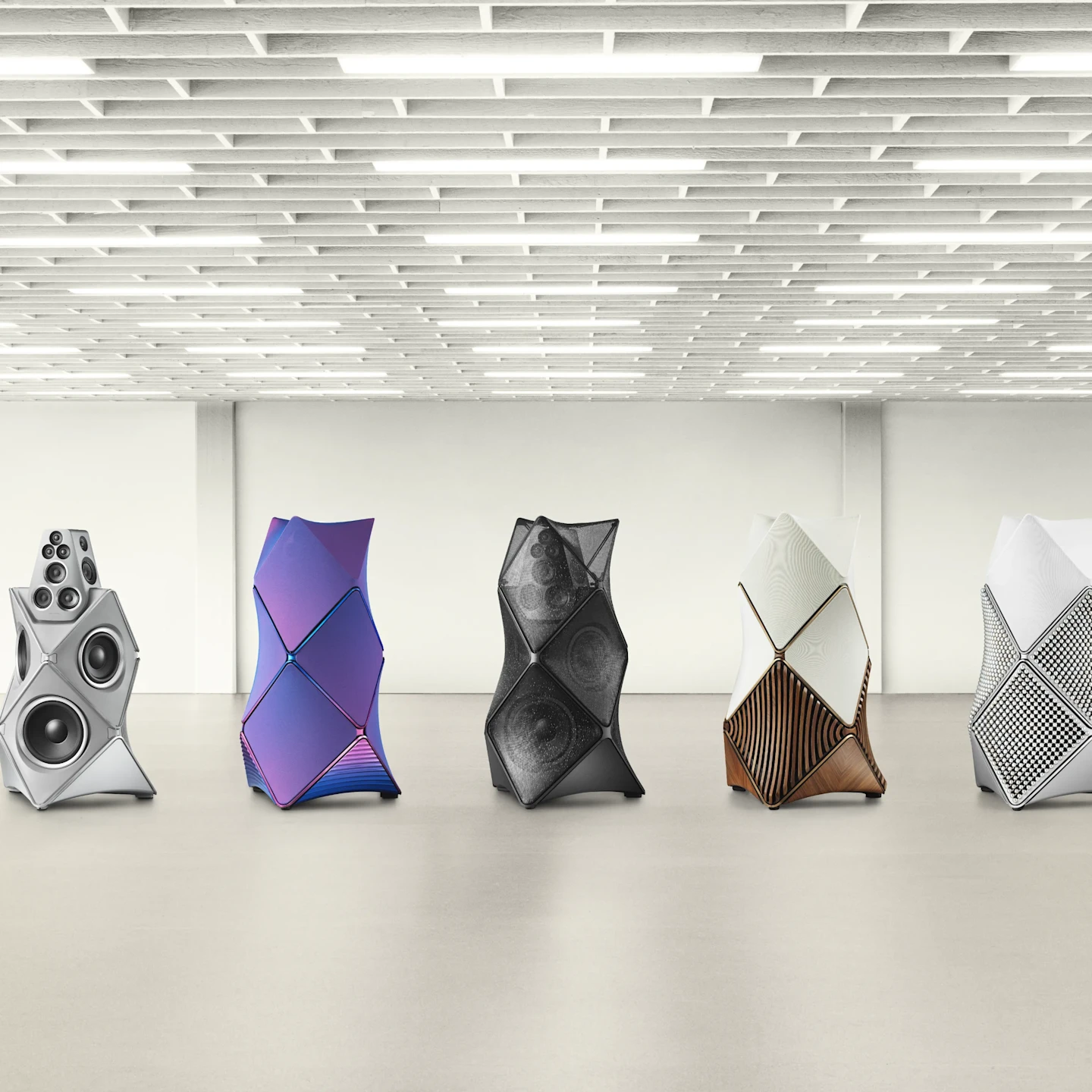 Row of futuristic speaker sculptures in a gallery with geometric, faceted designs in silver, purple, black, white, and bronze tones.
