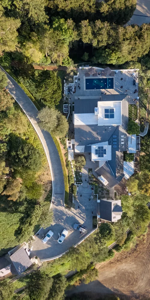 Aerial view of a suburban property with a rectangular blue pool, white deck, and surrounding trees and patios.