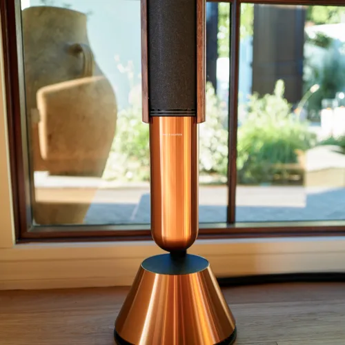 Beolab 28 floor-standing speaker with a black fabric cover, positioned by glass doors in a bright room.