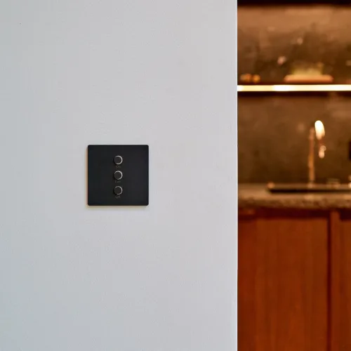 Lutron Alisse keypad with three circular buttons labeled On, Dim, Off mounted on a pale gray wall; warm kitchen scene visible to the right.