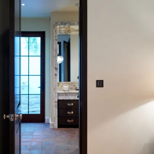 Hallway scene with a dark wooden doorframe; reflection shows a bathroom vanity with a marble top and a globe light.