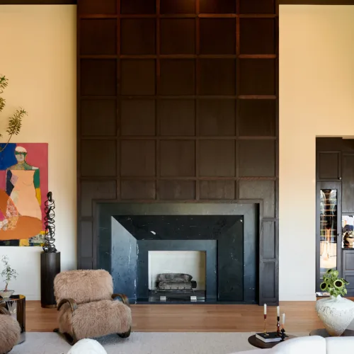 Living room with a tall dark wood-paneled fireplace wall, cream sectional seating, and round wooden coffee tables.