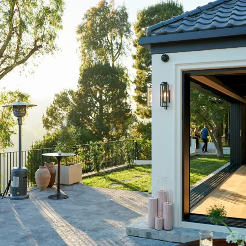 Outdoor patio with a round table, candles, and modern terrace overlooking trees and a sunny yard.