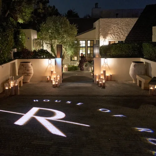 Nighttime courtyard entrance lit by candles along a path; a person stands near a doorway.